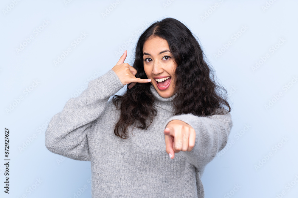 Spanish Chinese woman over isolated blue background making phone gesture and pointing front