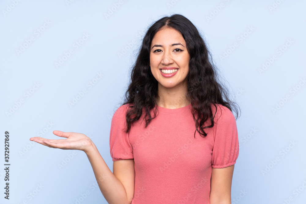Mixed race woman wearing a sweater over isolated blue background holding copyspace imaginary on the palm Mixed race woman wearing a sweater over isolated blue background holding copyspace imaginary on the palm