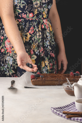 Woman holding blueberries over delicious cinnamon cake placed on white background.