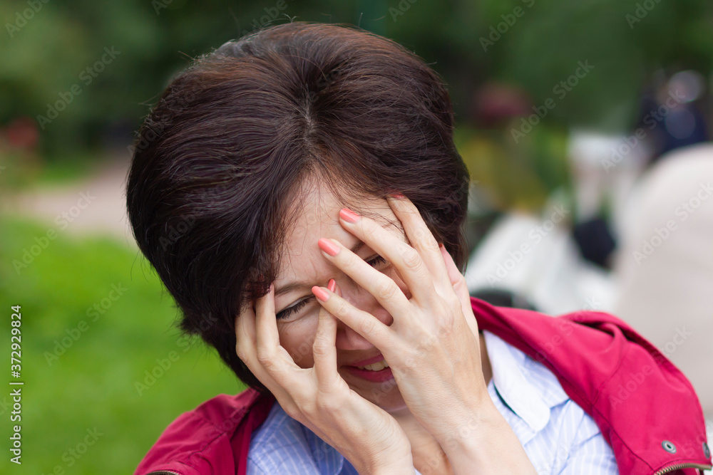 Beautiful positive emotional woman is smiling, laughing outdoors in a park, lady is covering her face with hands because of funny joke. Beautiful positive emotional woman is smiling, laughing outdoors in a park, lady is covering her face with hands because of funny joke.