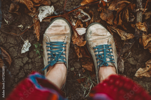 High angle personal view on ragged old shoes  walking on dry earth/ground with dry rust-coloured leaves, autumn/fall concept
