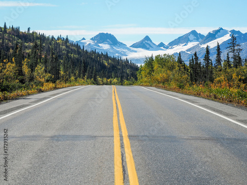 Asphalt road with yellow lines and the Worthington Glacier in Alaska in the background photo