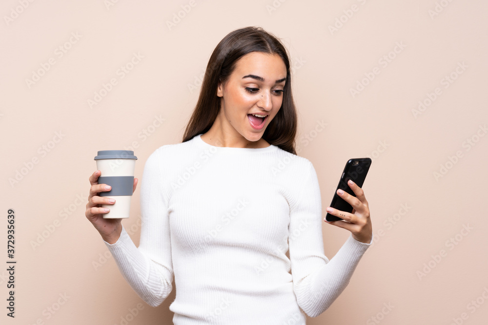 Young woman over isolated background holding coffee to take away and a mobile Young woman over isolated background holding coffee to take away and a mobile