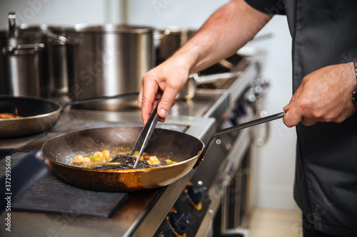 Chef cooking black spaghetti in a pan with tongs