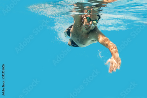 Pro male swimmer in the swimming pool. Underwater swim photo with copy space.