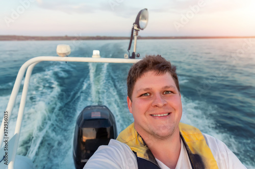 Young adult happy caucasian excited man portrait enjoy having fun driving fast motorboat on pond water surface at sunset evening time. Male person sailing fishing on speedboat by lake in morning photo