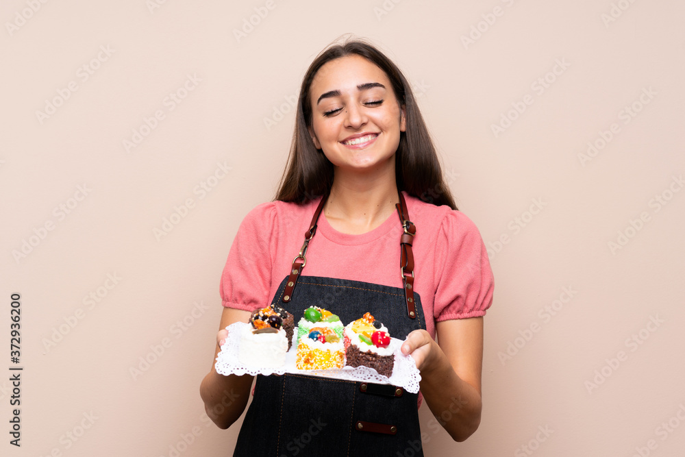 Young woman over isolated background holding mini cakes Young woman over isolated background holding mini cakes