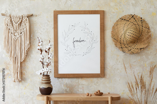 Beige boho interior of living room with mock up poster frame, elegant accessories, dried flowers in vase, wooden console and hanging rattan hut in stylish home decor.