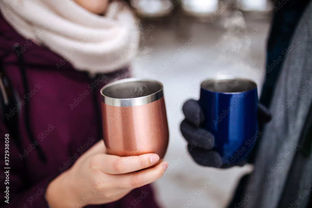 Two people hold thermo mugs with hot steaming tea