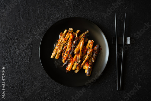 Eggplant slices in a spicy red sauce decorated black sesame seeds on dark concrete background. Top view. Asian food