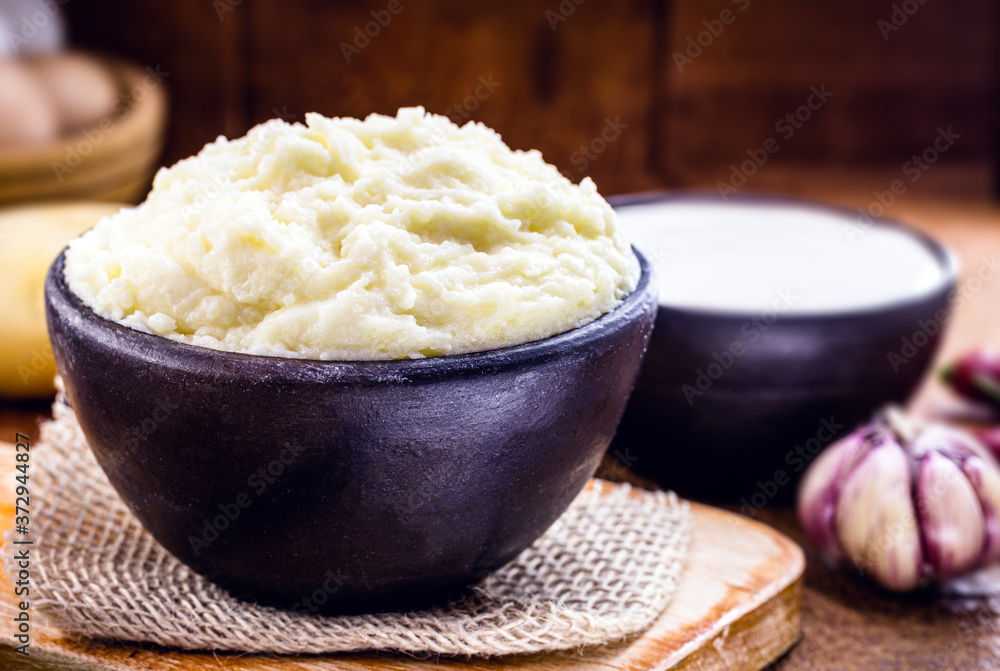 mashed potatoes or cream served in a handmade clay pot, with sour cream in the background on a rustic wooden table. Organic product. mashed potatoes or cream served in a handmade clay pot, with sour cream in the background on a rustic wooden table. Organic product.