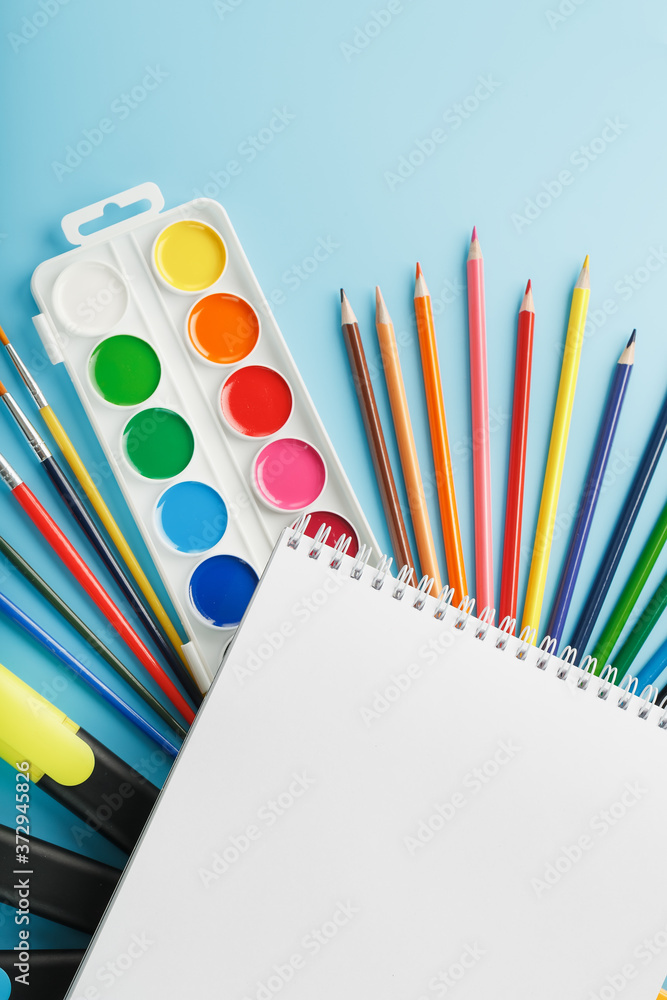 Fototapeta premium An album for drawing and creativity for school with stationery, a palette of colored paints, markers, brushes and pencils.
