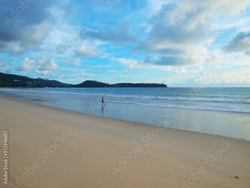 Bright blue sky with beautiful clouds, sandy beach, tropical resort. Man goes to the water. People swim in a sea. Seascape. Vacationing tourists. Clean sand, reflection from a water surface. Paradise