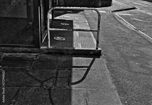A black and white image of sunlight and shadows on a sidewalk in the town of Stroud  England.