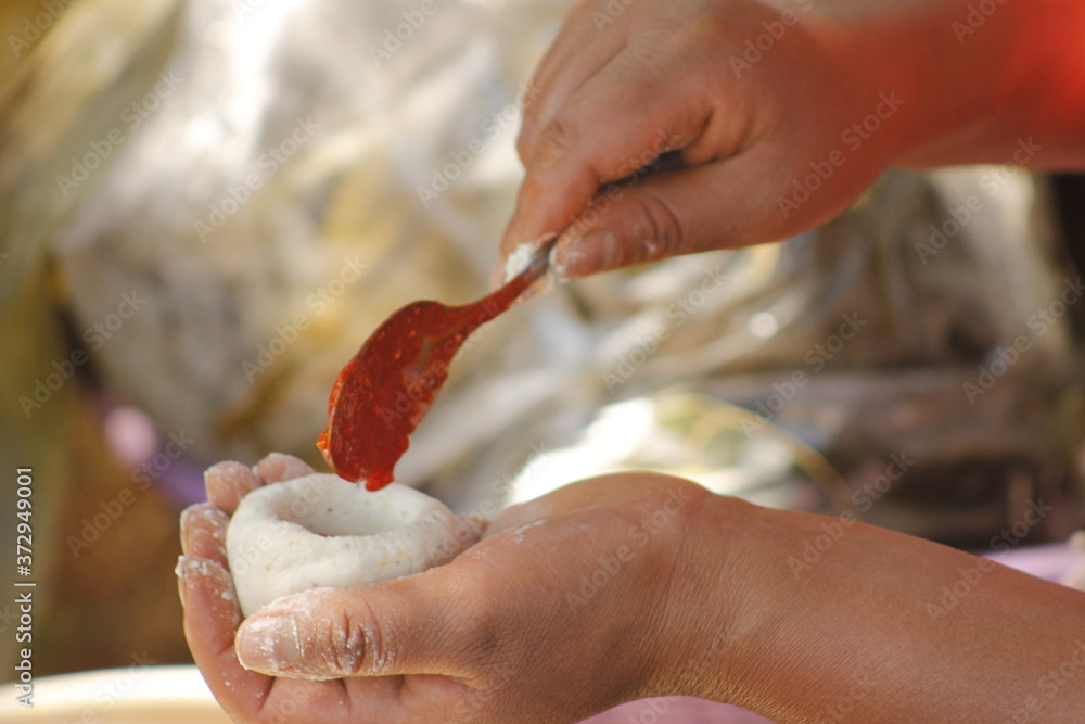 hands of indigenous woman adding red sauce to make Mexican tamales called corundas
