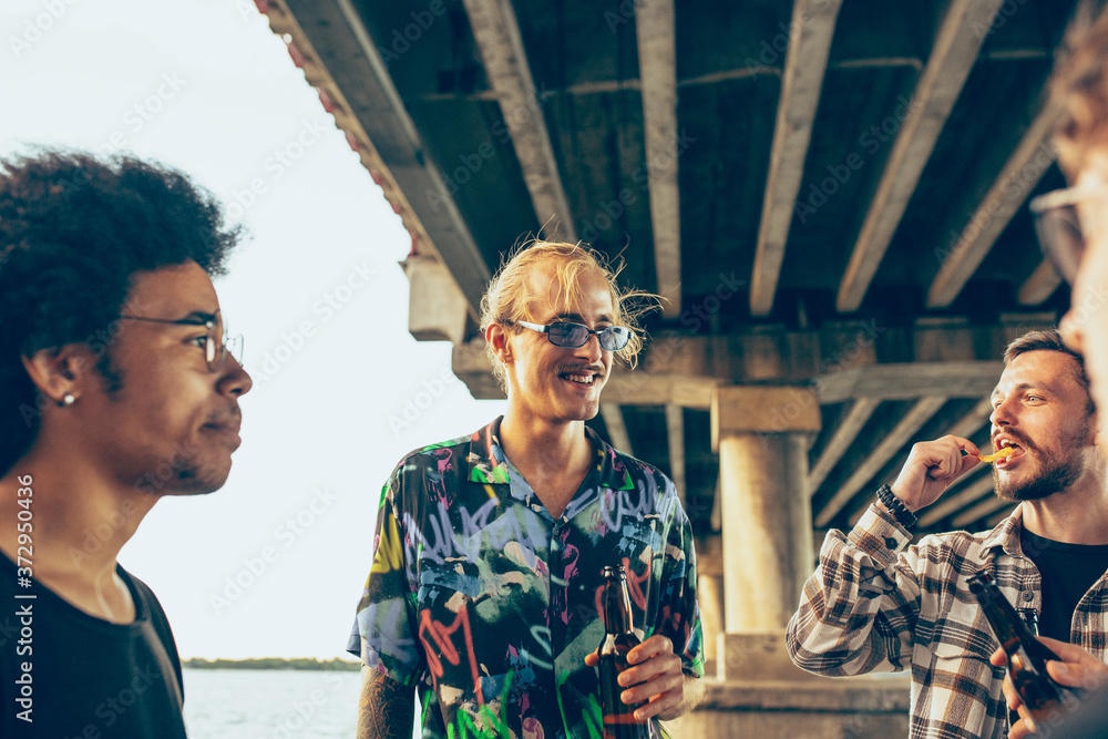 Group of friends celebrating, resting, having fun and party in summer day. Young men drinking beer, talking, laughting. Look happy and cheerful. Festive time, holiday, summertime, unity and friendship