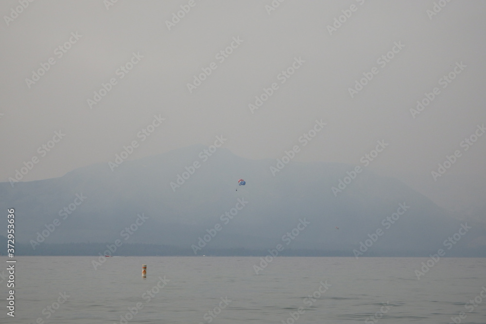 Smokey Skies Over Lake Tahoe with Parasailer in Foreground and Surrounding Western Sierras from Nevada Beach Nevada in from Wildfires of August 2020 Smokey Skies Over Lake Tahoe with Parasailer in Foreground and Surrounding Western Sierras from Nevada Beach Nevada in from Wildfires of August 2020