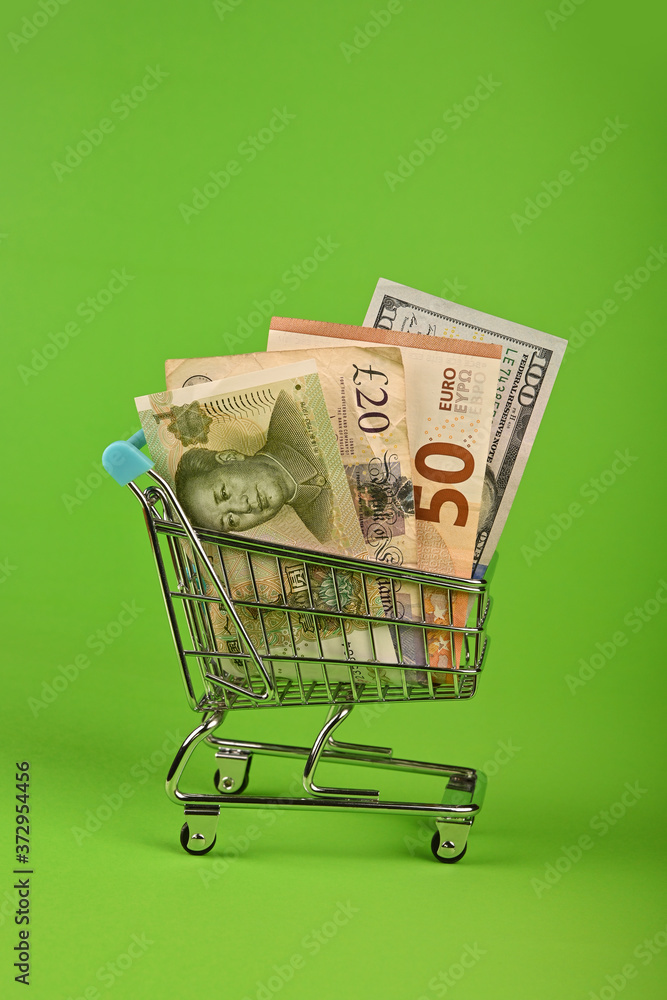 World paper currencies in shopping cart over green