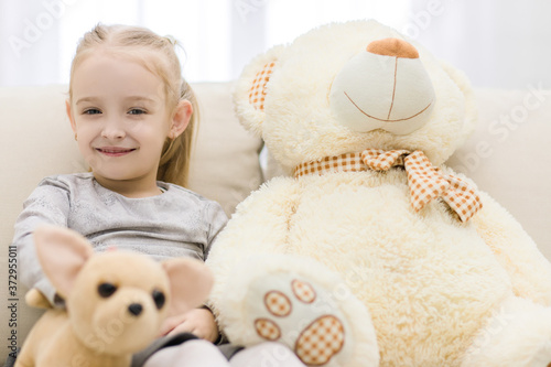 Photo where little girl sitting on white coach with her toy.