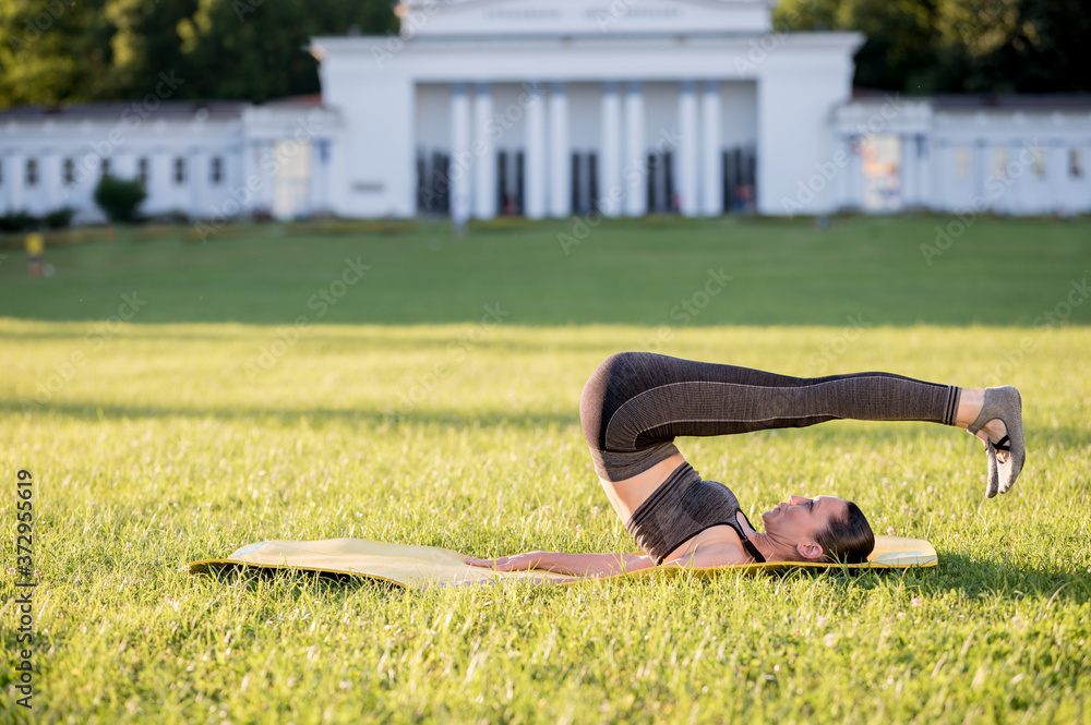 Fototapeta premium Beautiful young woman lying on a yellow mattress doing pilates or yoga, rolling back intermediate exercises