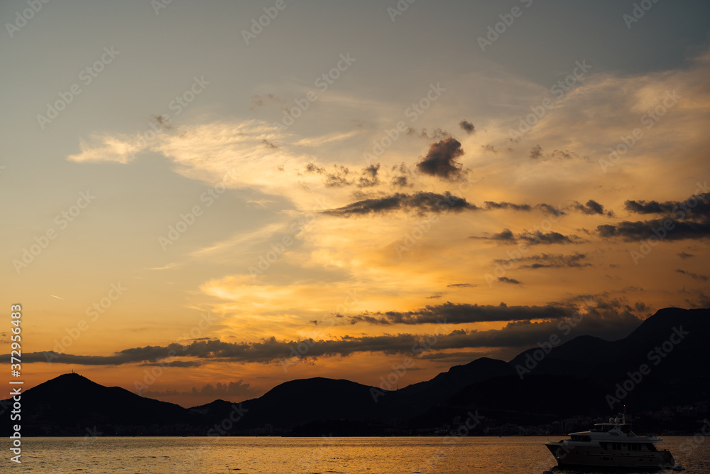 Dramatic fiery orange sunset sky over the sea and silhouettes of mountains.