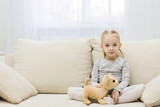 Adorable little girl of european appearance sitting on comfortable couch.