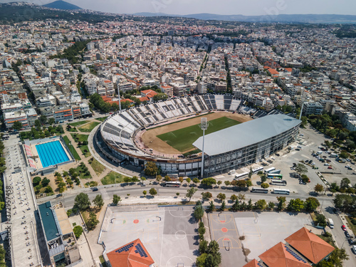 Thessaloniki, Greece landscape drone shot of PAOK FC Toumba stadium. Aerial top day view of empty football court with green pitch and team name written on the stands.