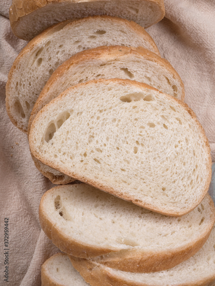 Sliced homemade white wheat bread with wheat flour on old wood tray on grey background. Top view. bread cloth. baton. napkin