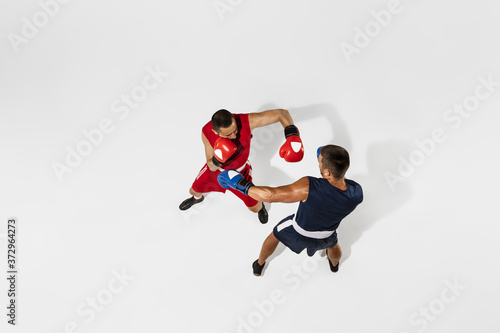 Two professional boxers boxing isolated on white studio background, action, top view. Couple of fit muscular caucasian athletes fighting. Sport, competition, excitement and human emotions concept. photo