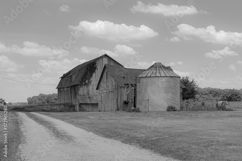 Broken down black and white barn with silo in the country.