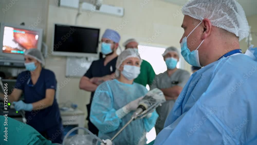 Surgery with modern medical equipment. Medical specialists in masks observe the surgical process on monitors. Medical team in operating room. Surgery with modern medical equipment. Medical specialists in masks observe the surgical process on monitors. Medical team in operating room.