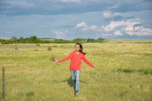 A girl with a bouquet of flowers runs across the field in the summer.