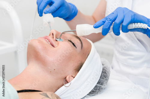 The young female client of cosmetic salon having microcurrent procedure on her face with special devices, close-up. Beautician using electrical impulses for facial procedures