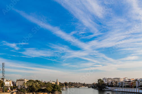 Blue sky with white clouds with an urban landscape, the Guadalquivir river on a sunny day in Seville, Spain © Emile