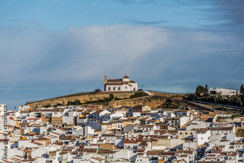 Obraz premium Church on a hill and white houses around in the village of Antequera, wonderful day with a blue sky in the province of Malaga Spain