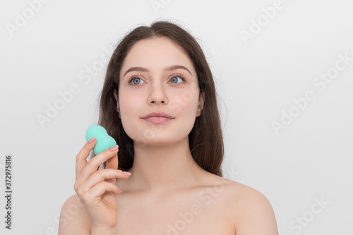 A young girl with a turquoise sponge for makeup. Looks up thoughtfully. Young girl with long hair and blue eyes.