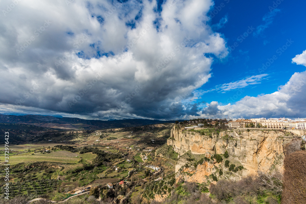 Panoramic view of the city of Ronda over the mountain with its valley with farmland and mountains in the background, wonderful sunny day with white clouds in the province of Malaga Spain