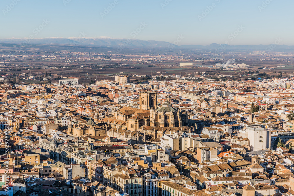 Aerial view of the city of Granada highlighting its cathedral (Capilla Real de Granada) or the Cathedral of the Incarnation and mountains in the background, sunny day with a blue sky in Spain