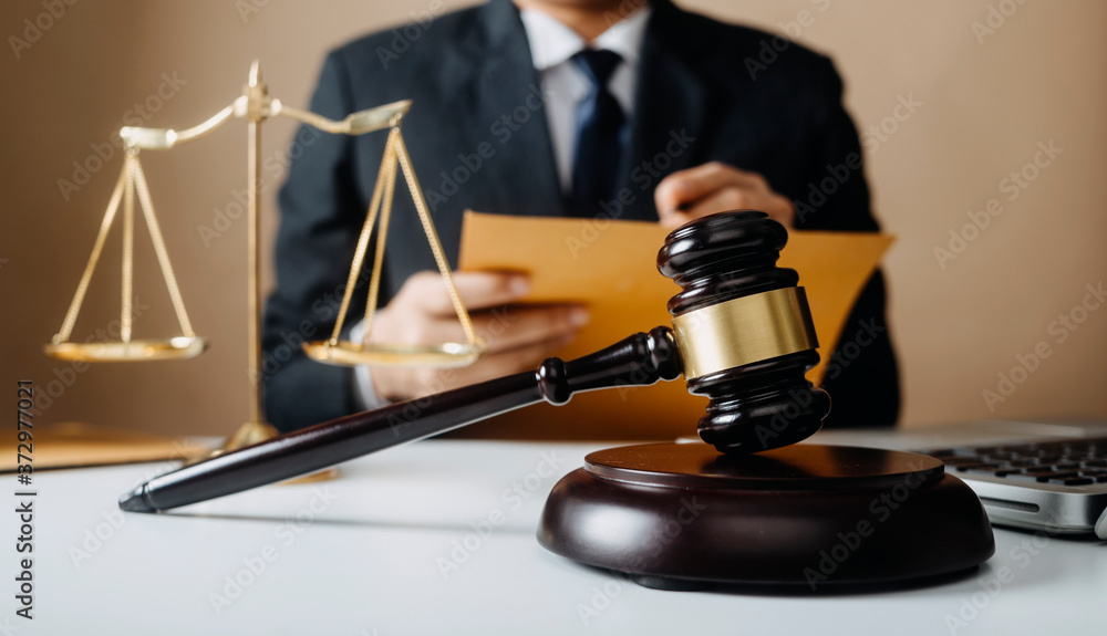 Justice and law concept.Male judge in a courtroom with the gavel, working with, computer and docking keyboard, eyeglasses, on table in morning light Justice and law concept.Male judge in a courtroom with the gavel, working with, computer and docking keyboard, eyeglasses, on table in morning light