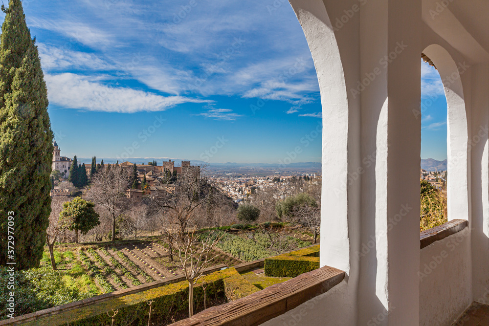 Orchards next to leafless trees seen from a balcony with the Alhambra and the city of Granada in the background, sunny winter day in Spain