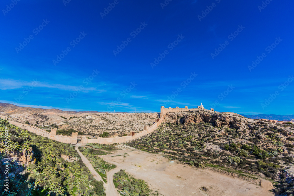 Panoramic view of a rocky and arid mountainous terrain with the walls of the Alcazaba of Almeria, sunny day with a clear blue sky in the municipi de Andalucia, Spain