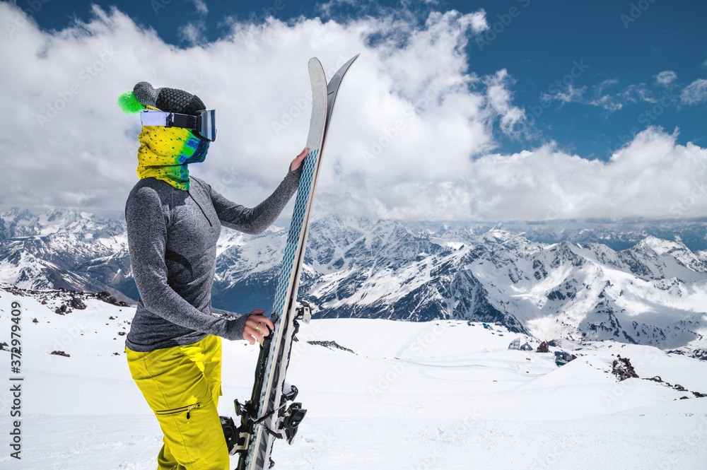 Portrait of a women skier without jacket in a ski mask with her face closed on a sunny day against the backdrop of snow-capped Caucasian mountains and clouds Portrait of a women skier without jacket in a ski mask with her face closed on a sunny day against the backdrop of snow-capped Caucasian mountains and clouds