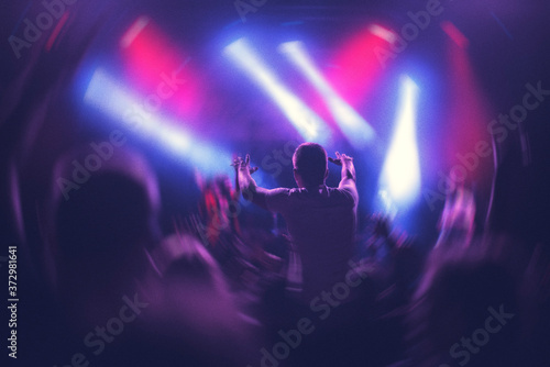 Hombre joven divirtiéndose en festival, en uno de los conciertos, con las dos manos arriba y luces rojas y azules de fondo photo