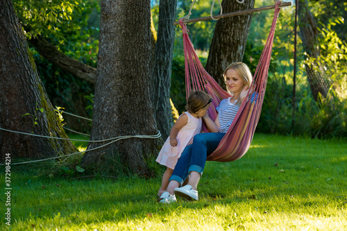 A young woman with a small child is sitting in a hammock in her garden.