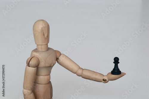 Wooden figurine holds black pawn in his hand