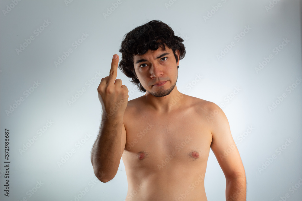 Fototapeta premium Young naked hispanic man with wavy hair and shaved beard, with angry expression, using the middle finger sign