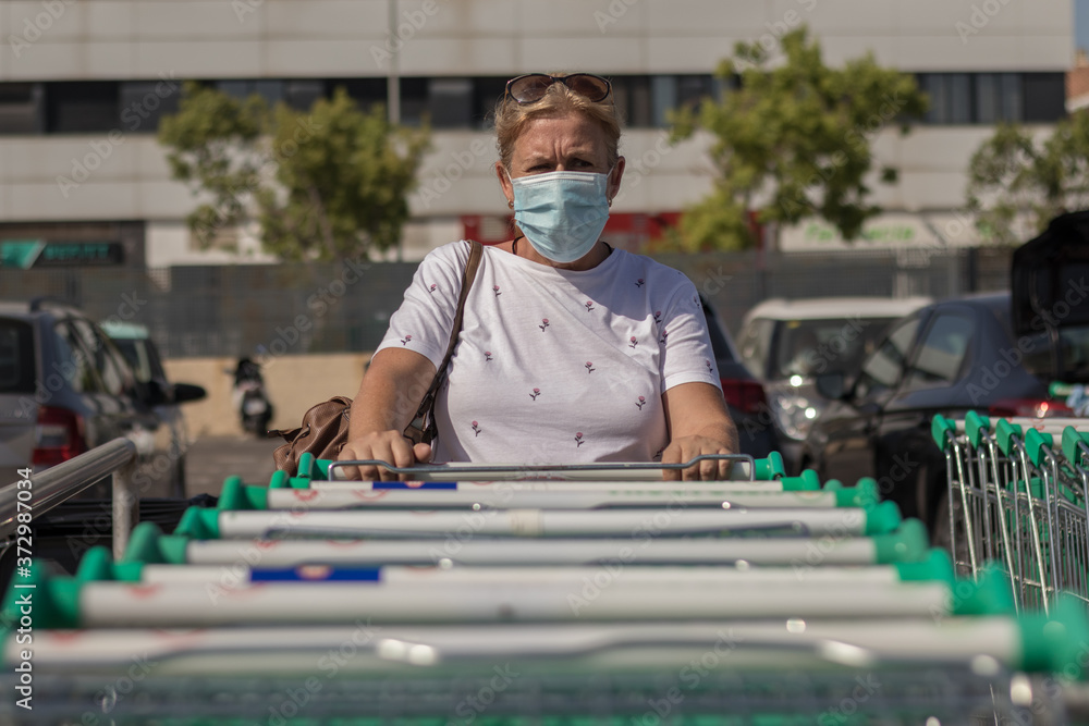 Mujer con mascarilla cogiendo un carro para comprar en un supermercado Stock Photo | Adobe Stock