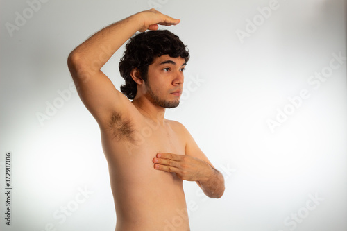 Young naked hispanic man with wavy hair and shaved beard, doing a checkup on his chest for signs of breast cancer