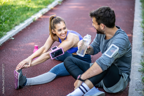 A couple on a treadmill in nature, woman doing leg stretching exercises while man sits and drink water
