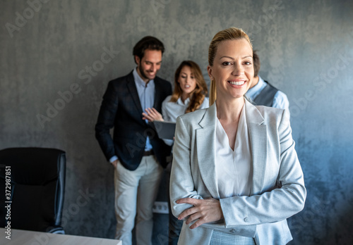 Business woman standing in front of their colleagues, smiling and looking at the camera with crossed arms